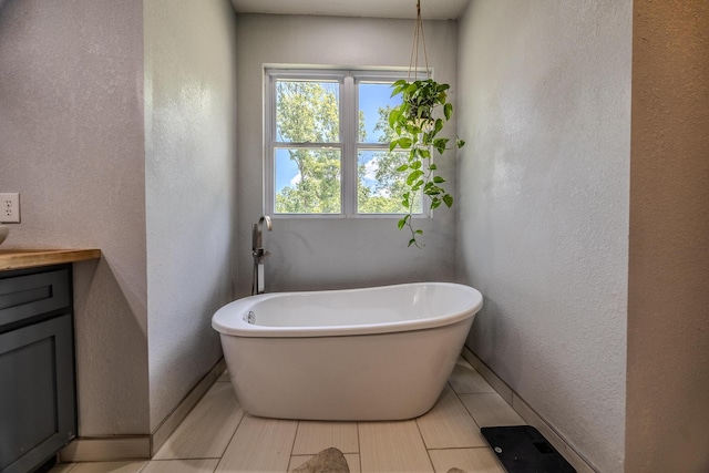 bathroom featuring a soaking tub, baseboards, a textured wall, and vanity