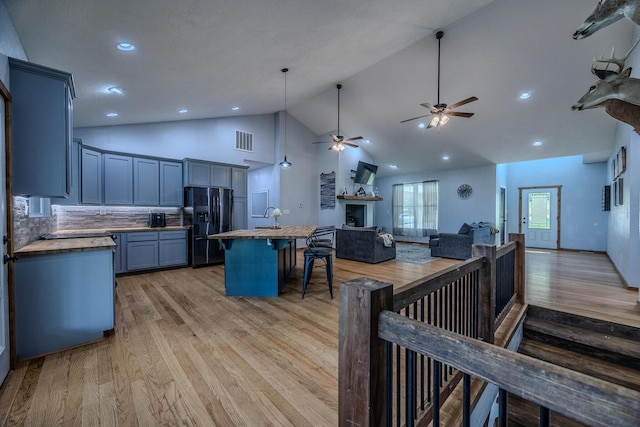 kitchen with butcher block counters, visible vents, black refrigerator with ice dispenser, light wood-style flooring, and open floor plan