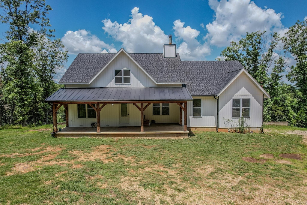 back of house featuring metal roof, roof with shingles, a lawn, a standing seam roof, and a chimney