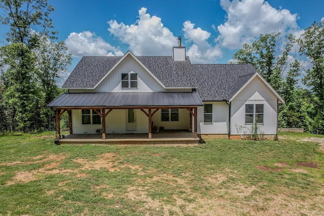 back of house featuring metal roof, roof with shingles, a lawn, a standing seam roof, and a chimney