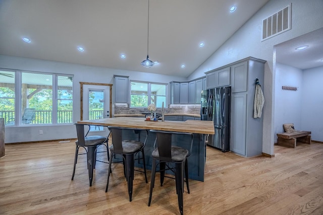 kitchen with light wood finished floors, butcher block counters, visible vents, black refrigerator with ice dispenser, and backsplash