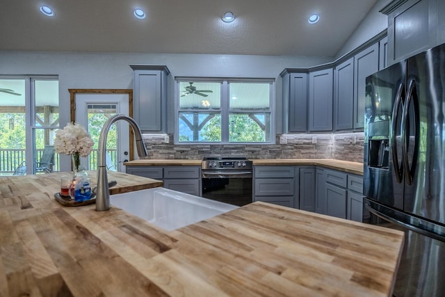 kitchen featuring stainless steel electric range oven, tasteful backsplash, black fridge with ice dispenser, a sink, and wood counters