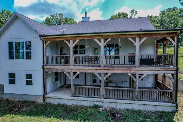 back of house with a shingled roof, a patio area, and a chimney