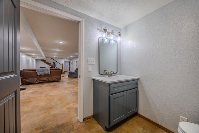 bathroom with baseboards, a textured wall, toilet, concrete flooring, and vanity