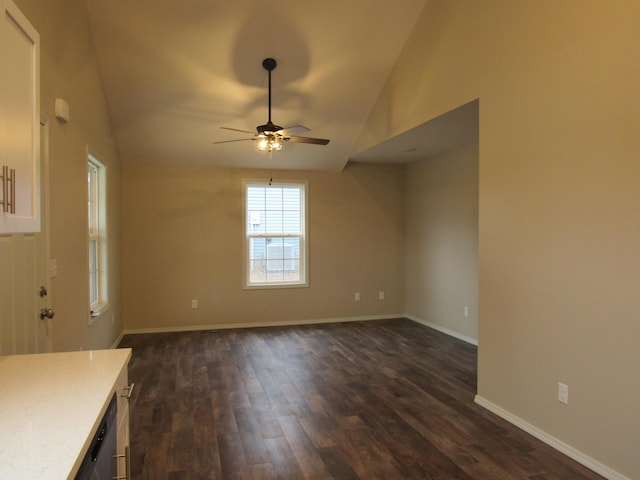 empty room featuring a ceiling fan, baseboards, vaulted ceiling, and dark wood finished floors