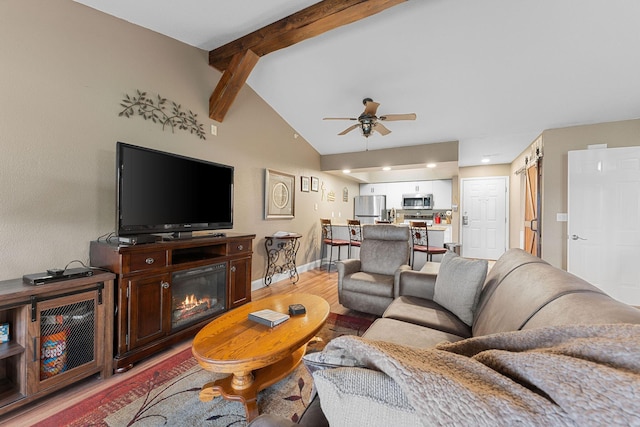 living room featuring baseboards, lofted ceiling with beams, ceiling fan, a glass covered fireplace, and light wood-type flooring