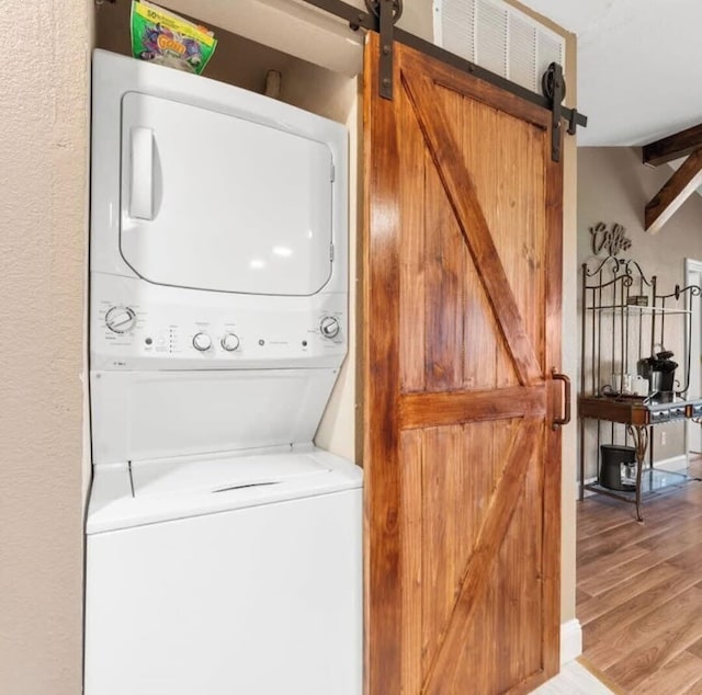 washroom featuring a barn door, light wood-type flooring, stacked washer / drying machine, and laundry area