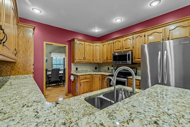 kitchen with light stone counters, stainless steel appliances, wood finished floors, a sink, and brown cabinetry