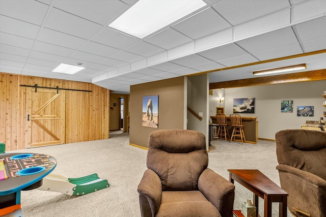 rec room featuring a barn door, a drop ceiling, carpet flooring, a bar, and wood walls