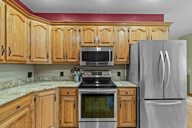 kitchen with appliances with stainless steel finishes, backsplash, and light stone counters