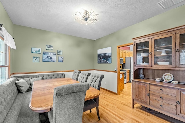 dining space with a textured ceiling, light wood finished floors, visible vents, and baseboards