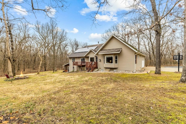 view of front facade featuring a fire pit, solar panels, a front yard, and a wooden deck