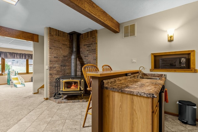 bar featuring light colored carpet, a sink, visible vents, beam ceiling, and a wood stove