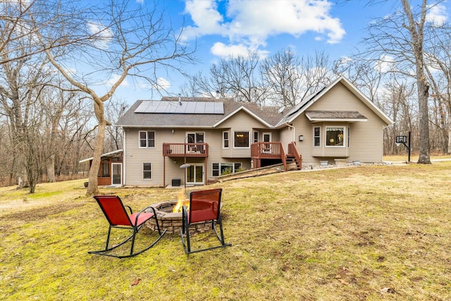 rear view of house with roof with shingles, a yard, roof mounted solar panels, a deck, and a fire pit