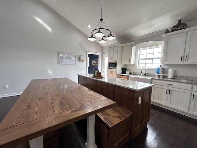 kitchen featuring lofted ceiling, a sink, a kitchen island, white cabinets, and stainless steel microwave