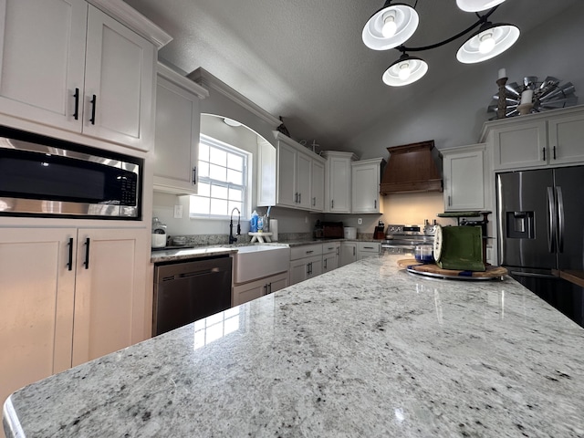 kitchen with lofted ceiling, appliances with stainless steel finishes, light stone counters, premium range hood, and a sink