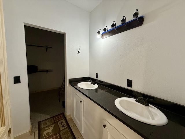 full bath with double vanity, tile patterned flooring, a walk in closet, and a sink