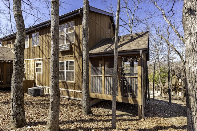 view of property exterior featuring a shingled roof, board and batten siding, central AC unit, and a sunroom