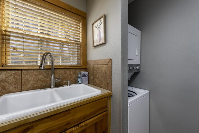 laundry room featuring stacked washer and clothes dryer, a sink, and laundry area