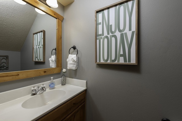 bathroom with vaulted ceiling, a textured ceiling, and vanity