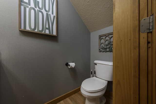 bathroom featuring baseboards, toilet, wood finished floors, vaulted ceiling, and a textured ceiling