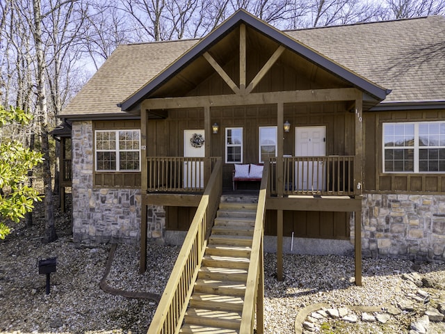 doorway to property featuring a shingled roof, stone siding, covered porch, and board and batten siding