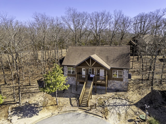 rustic home featuring a deck, stone siding, roof with shingles, and stairway