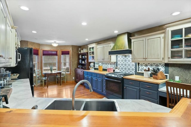 kitchen featuring custom exhaust hood, tasteful backsplash, gas stove, a sink, and blue cabinets