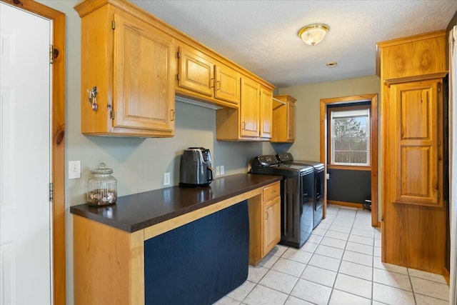 kitchen with dark countertops, light tile patterned flooring, a textured ceiling, and washing machine and clothes dryer