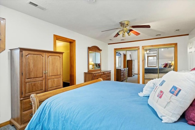 carpeted bedroom with multiple closets, visible vents, ceiling fan, and ornamental molding