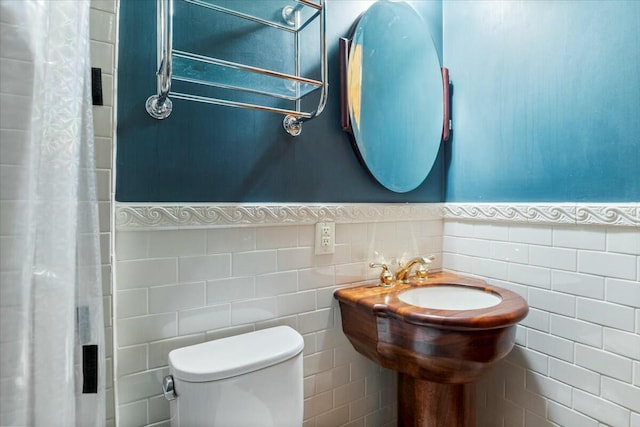 bathroom with a shower with shower curtain, wainscoting, toilet, and tile walls