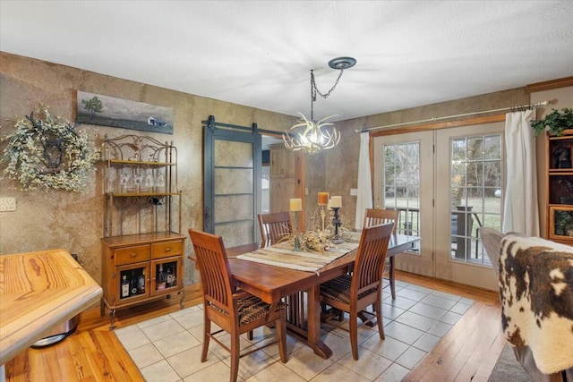 dining space with light wood-type flooring, a notable chandelier, and a barn door