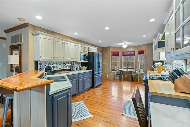 kitchen featuring a peninsula, a sink, visible vents, light wood-type flooring, and stainless steel microwave