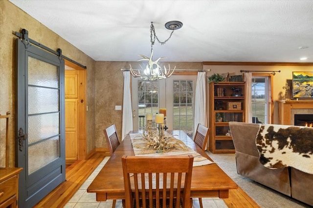 dining space with an inviting chandelier, a barn door, a fireplace, and light wood-style floors