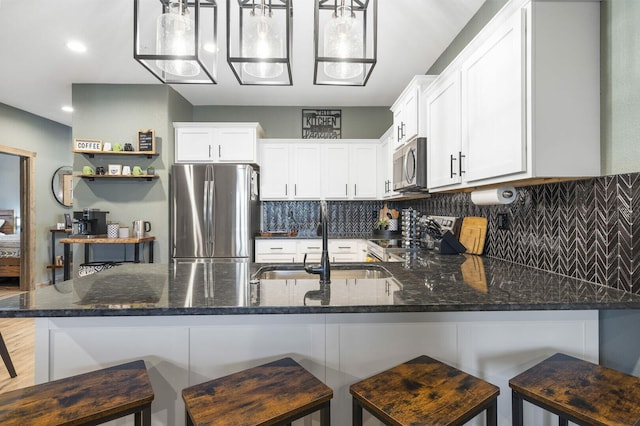 kitchen featuring tasteful backsplash, dark stone counters, appliances with stainless steel finishes, white cabinetry, and a sink