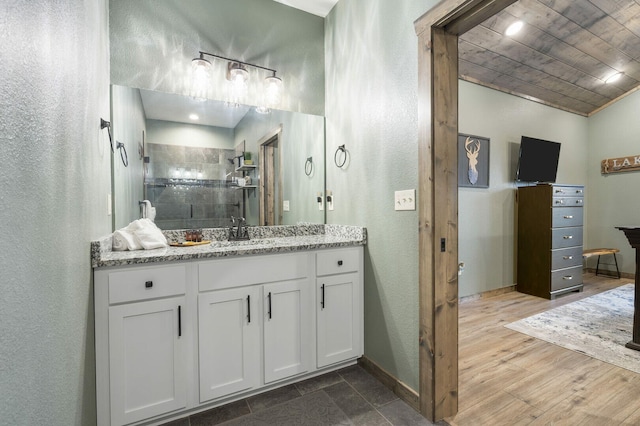 bathroom featuring wood ceiling, vanity, wood finished floors, tiled shower, and baseboards