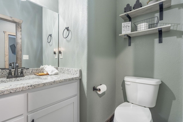 half bath with a textured wall, vanity, and toilet