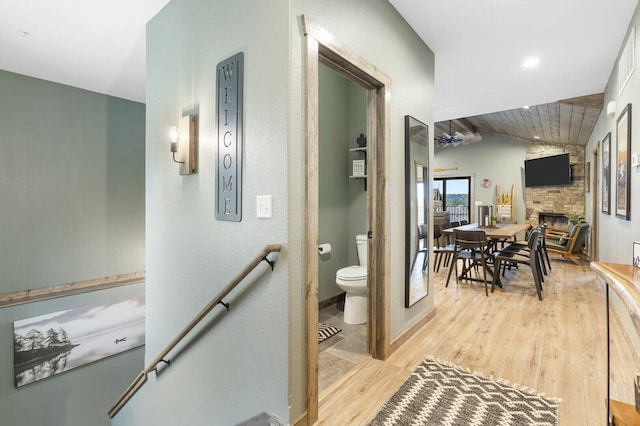 corridor with vaulted ceiling, light wood finished floors, and an upstairs landing