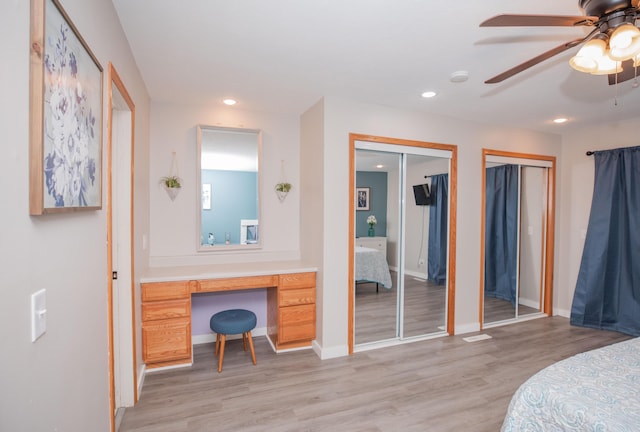 bedroom with light wood-type flooring, built in study area, recessed lighting, and two closets