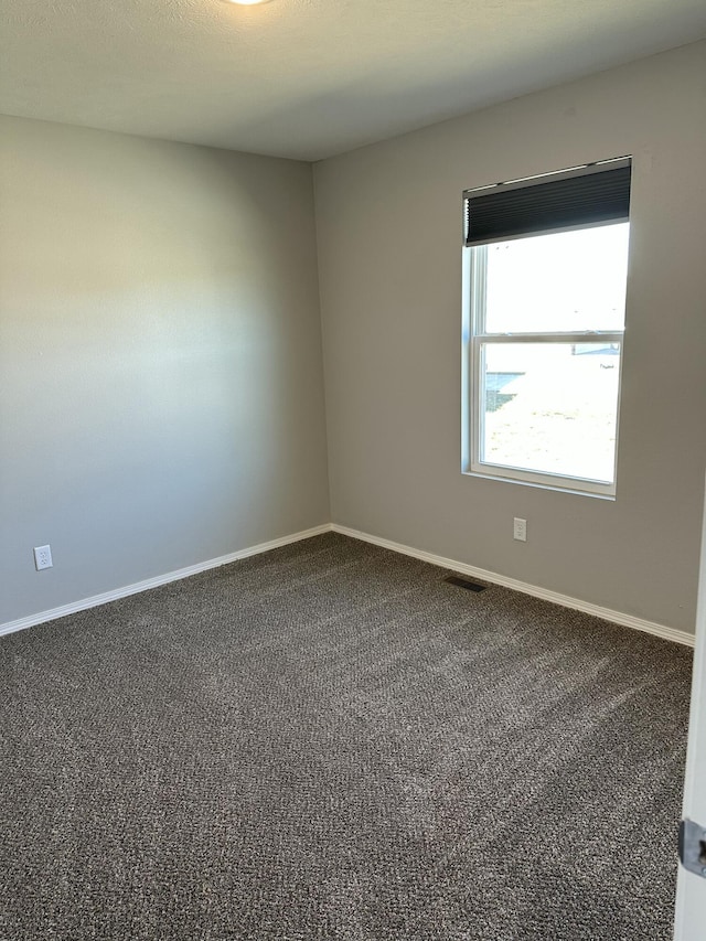 unfurnished room with dark carpet, visible vents, and baseboards