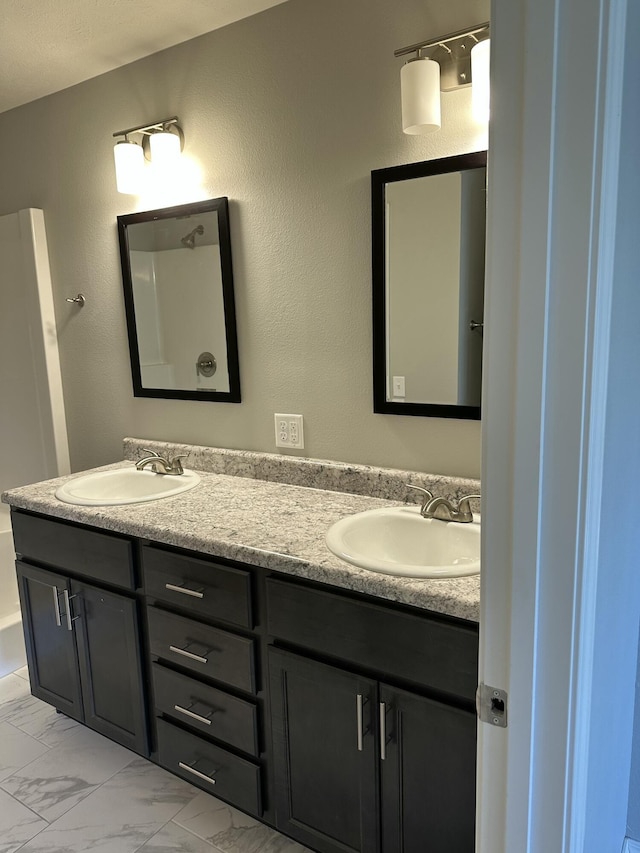 full bath with marble finish floor, double vanity, and a sink