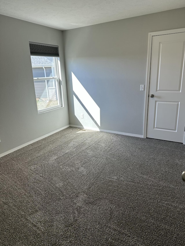 carpeted spare room with a textured ceiling and baseboards