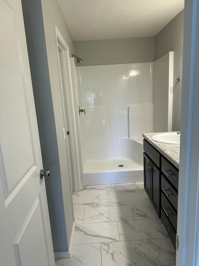 full bath with a shower, marble finish floor, a textured ceiling, vanity, and baseboards