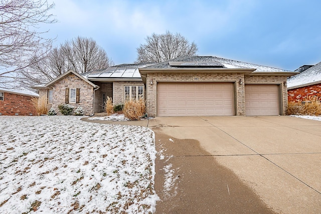 view of front of property featuring driveway, a garage, solar panels, and brick siding