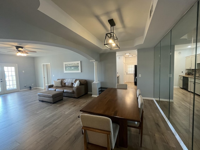 dining room featuring arched walkways, a raised ceiling, baseboards, and wood finished floors