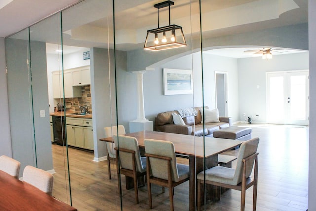 dining room with baseboards, decorative columns, light wood-style flooring, arched walkways, and a ceiling fan