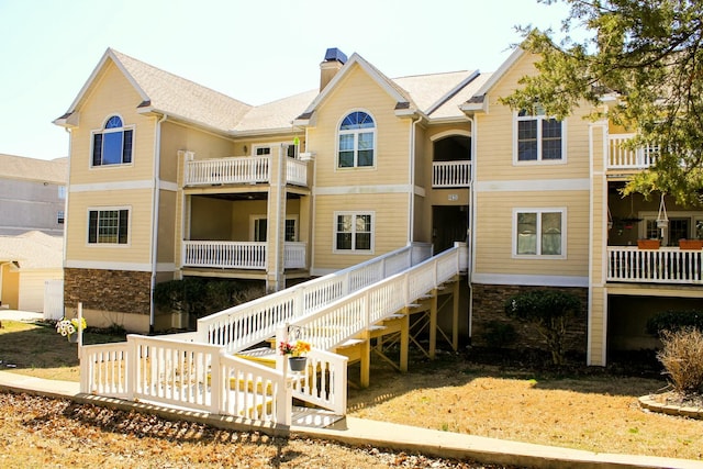 back of house featuring stairs, stone siding, and a chimney