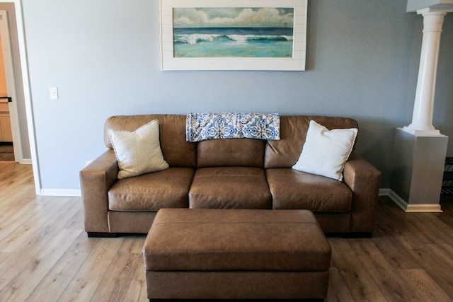 living room with light wood-type flooring, baseboards, and decorative columns