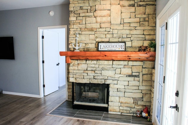 interior details with a stone fireplace, wood finished floors, and baseboards