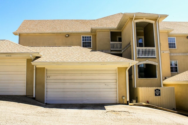 view of property with a garage, a balcony, a shingled roof, and stucco siding